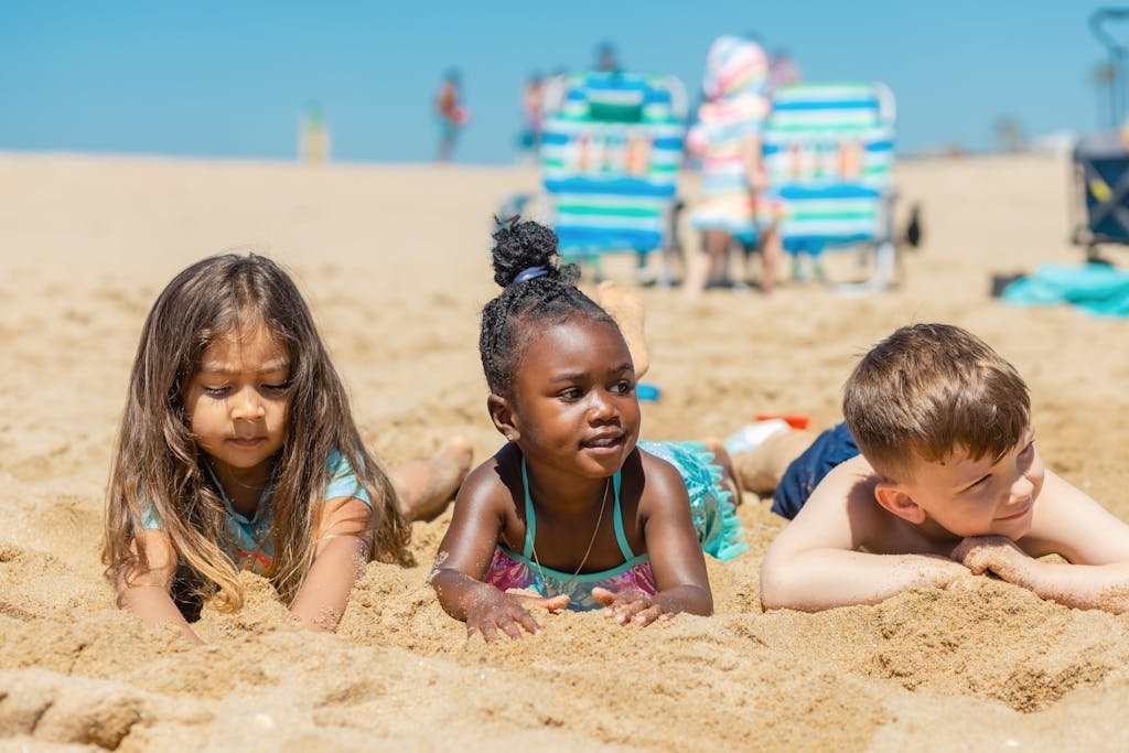 Three children enjoying a sunny day at the beach, playing in the sand.