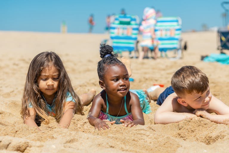 Three children enjoying a sunny day at the beach, playing in the sand.