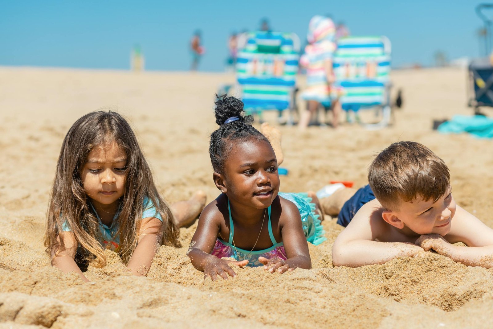 Three children enjoying a sunny day at the beach, playing in the sand.